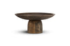 The nkuku Eisha Wooden Cake Stand in brown features a hand-carved, wide shallow dish on a sturdy cylindrical base. Its textured surface and natural grain patterns make it ideal for serving or as a rustic cake stand. Photographed on white background.