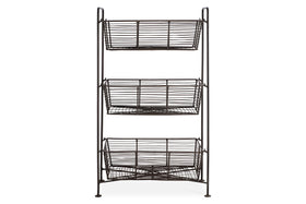 The nkuku Inkollu Three Tier Storage Stand in antiqued brass has rectangular open-wire baskets stacked vertically on a minimalist frame with four slender legs, ideal for kitchen organization and storage.