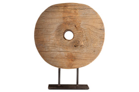 The Cala Reclaimed Wood Objet on Stand - Natural by nkuku features a round, flat wooden disk with a central hole, displayed upright on a simple black metal stand. Visible grain and cracks highlight its rustic charm against a plain white background.