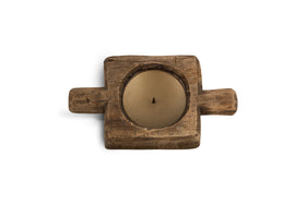 A tan round candle rests in the nkuku Apu Reclaimed Wood Traditional Candle Holder—natural finish, rustic square shape, two short handles, and hand-carved details—photographed from above on a white background.