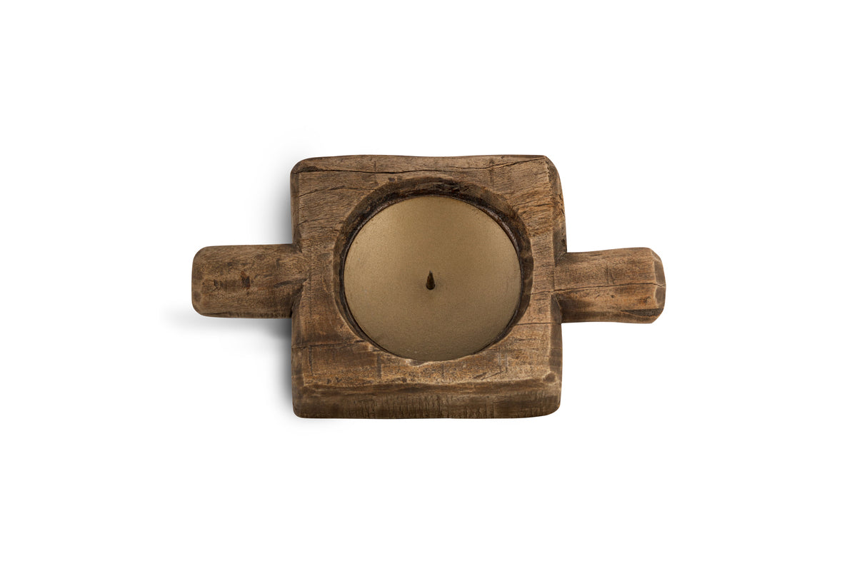 A tan round candle rests in the nkuku Apu Reclaimed Wood Traditional Candle Holder—natural finish, rustic square shape, two short handles, and hand-carved details—photographed from above on a white background.