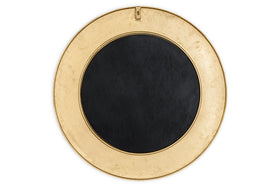 The Moto Round Mirror by nkuku features an antique brass finish and a wide border, with a small hanging hook at the top. This minimalist mirror rests against a plain white background, perfect for elegant decor.