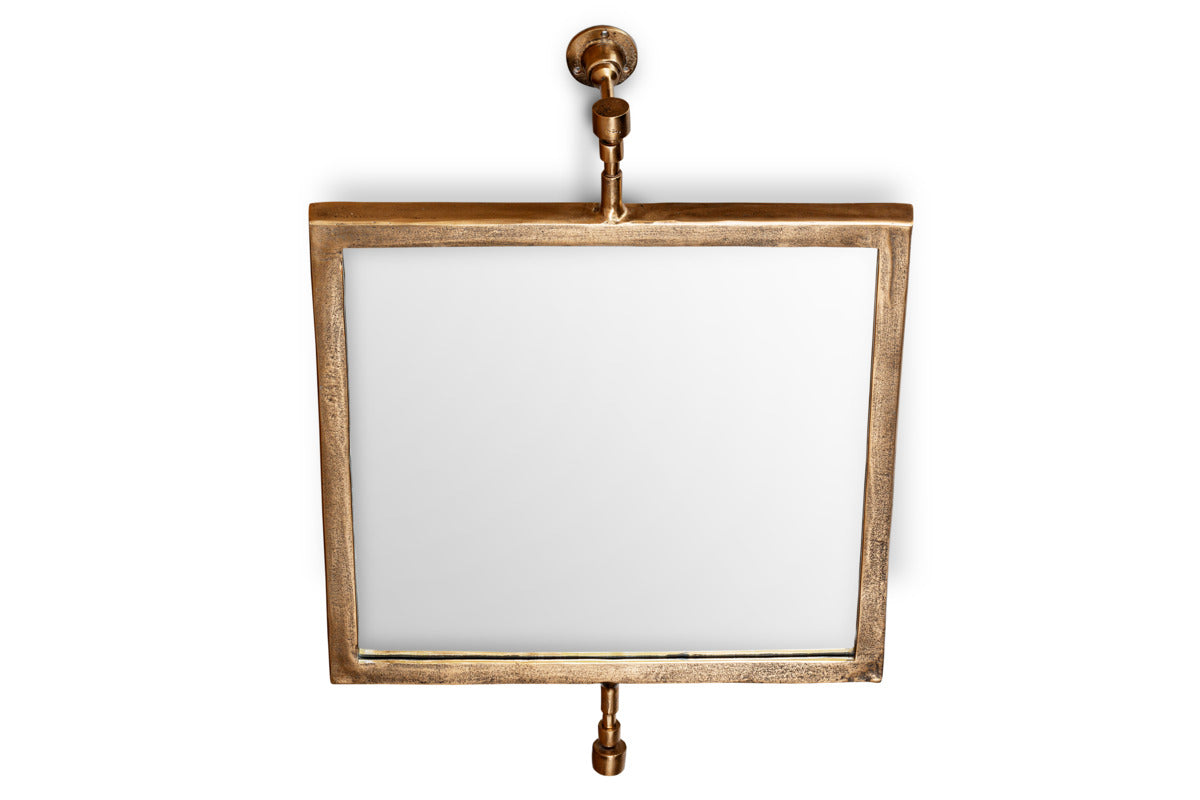 The Visala Swivel Wall Mirror by nkuku features a square, thick antique brass frame and pipe-style supports with exposed hardware, creating an industrial look against a white backdrop.