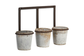 The nkuku Tukana Triple Wall Hung Planter - Zinc features three weathered galvanized pots with rustic patina, each hanging from a ring on a rectangular metal frame for an industrial accent wall display.