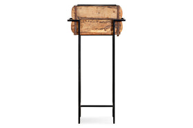 The nkuku Amazzi Indoor Planter Stand - Natural & Black features thin black metal legs and a crossbar, supporting a rustic reclaimed wooden planter box with a weathered finish, shown front-facing against a plain white background.