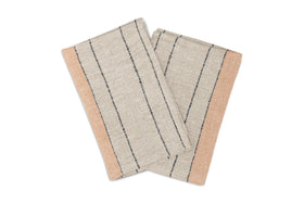 The Buna Placemats - Clay by nkuku are a set of two rectangular placemats in beige with a subtle herringbone pattern, thin black stripes, and broad tan borders, arranged overlapped in an X shape to enhance your table setting.