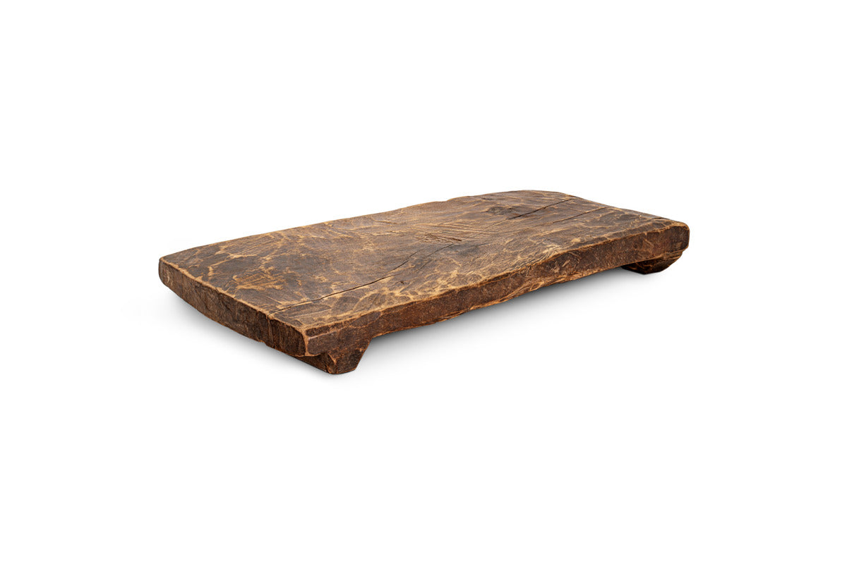 The Kaveeta Reclaimed Serving Board - Natural by nkuku is a rustic, rectangular wooden board made from reclaimed wood with a dark brown finish, visible grain, uneven surface and edges, and rests on two small feet.