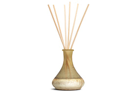 The nkuku Oakmoss & Rose Scented Reed Diffuser features a pear-shaped yellow ceramic vase with a matte finish, filled with light wooden reeds that diffuse a subtle floral fragrance into your space.