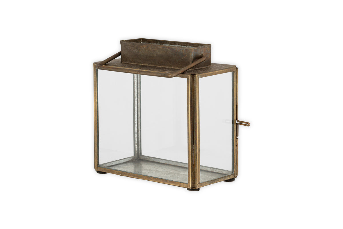 The Obi Mini Table Lantern by nkuku features an antique brass finish, a glass door, and handle—perfect for soft candlelight or as a charming decorative accent.