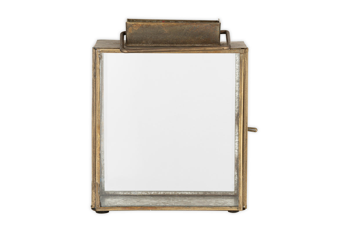 The nkuku Obi Mini Table Lantern in antique brass features a rectangular metal and glass design with a top handle, hinged glass door, and rustic finish—ideal for adding candlelight charm to any space. Shown against a white background.