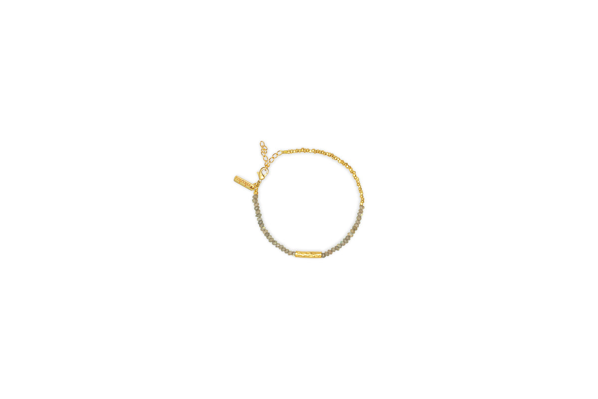 The Perdu Labradorite Bracelet - Gold by nkuku features small gray labradorite and gold brass beads, a gold bar centerpiece, and an adjustable clasp for a refined touch of natural stone elegance.