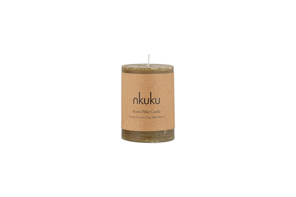 The Rustic Soy Blend Mini Pillar Candle - Olive by nkuku features a hand-poured, olive-toned soy wax blend, a textured finish, and a brown paper label. This mini rustic candle is shown against a white background.