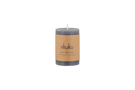 The Rustic Soy Blend Mini Pillar Candle - Charcoal by nkuku is a grey mini pillar candle with a textured finish and a brown label, shown against a white background.