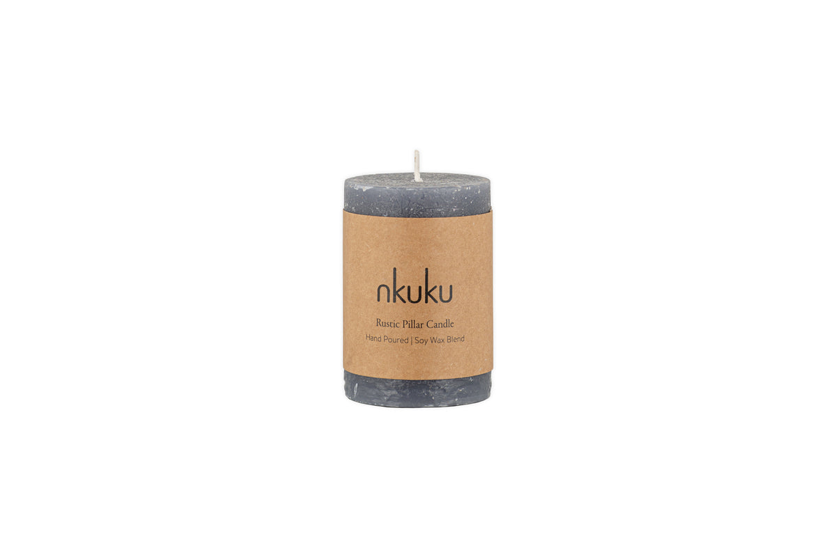 The Rustic Soy Blend Mini Pillar Candle - Charcoal by nkuku is a grey mini pillar candle with a textured finish and a brown label, shown against a white background.