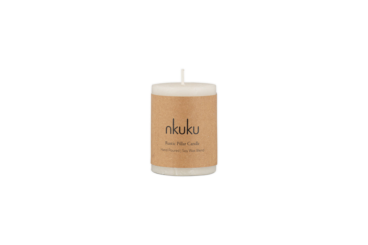 A white Rustic Soy Blend Mini Pillar Candle by nkuku, featuring a textured finish and a brown paper label, shown against a plain white background.