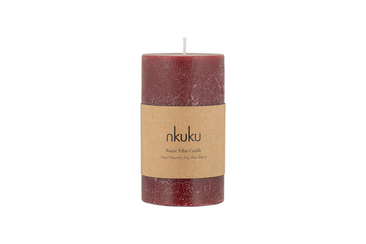 A small nkuku Rustic Soy Blend Pillar Candle in Dark Cherry with a textured finish and a brown paper label stands upright on a white background.