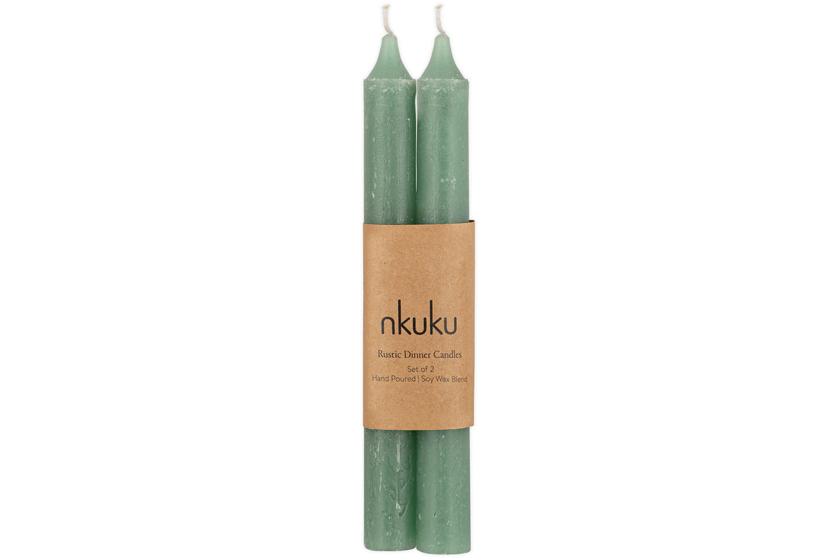The nkuku Rustic Soy Blend Dinner Candle - Sage Green (Set of 2) features two textured sage green candles with visible wicks, bundled together with a brown paper label.