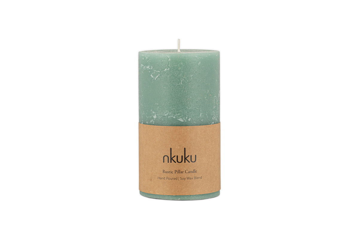 A small sage green Rustic Soy Blend Pillar Candle by nkuku, featuring a textured finish and a brown label, is shown against a white background.