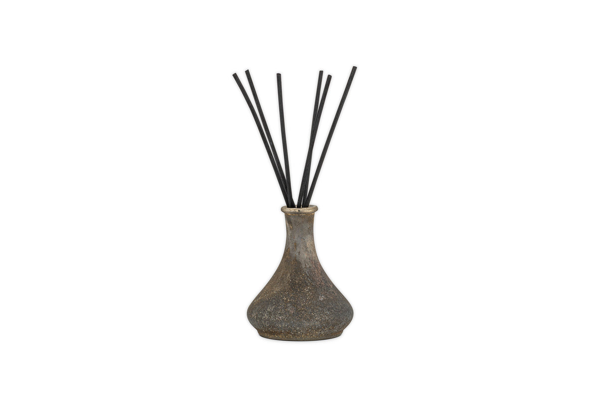 The nkuku Cedarwood & Fig Reed Diffuser features a rustic, speckled ceramic bottle with a narrow neck and black reeds, ideal for spreading a soothing cedarwood scent.