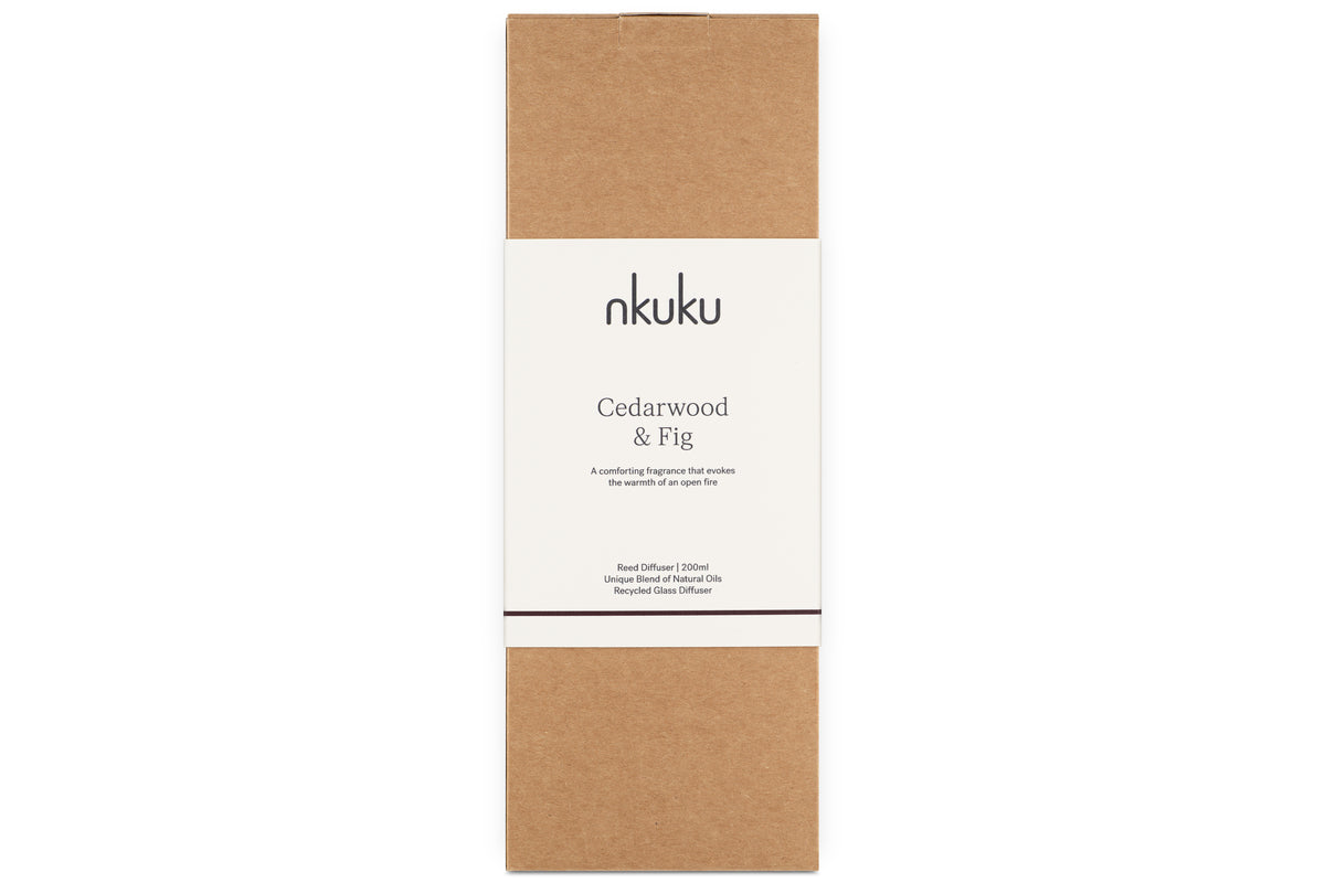 A rectangular box with a brown base and a white label featuring the nkuku brand. The label reads Cedarwood & Fig Reed Diffuser, describing the inviting cedarwood fragrance inside.