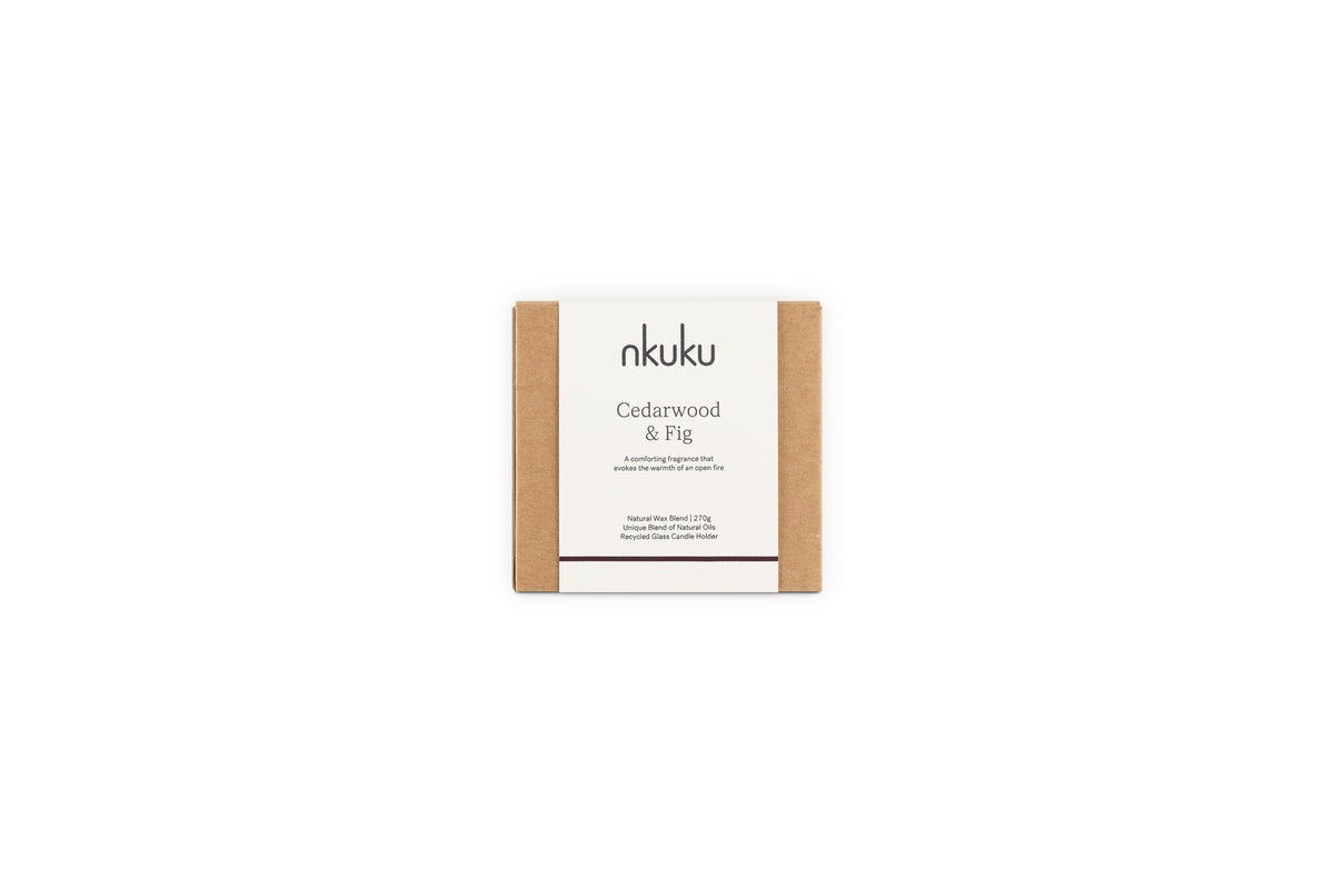 The nkuku Cedarwood & Fig 1 Wick Scented Candle, in minimalist packaging with a white label and brown kraft paper sides, fills the air with a warm honeyed fig aroma when displayed against a plain white background.