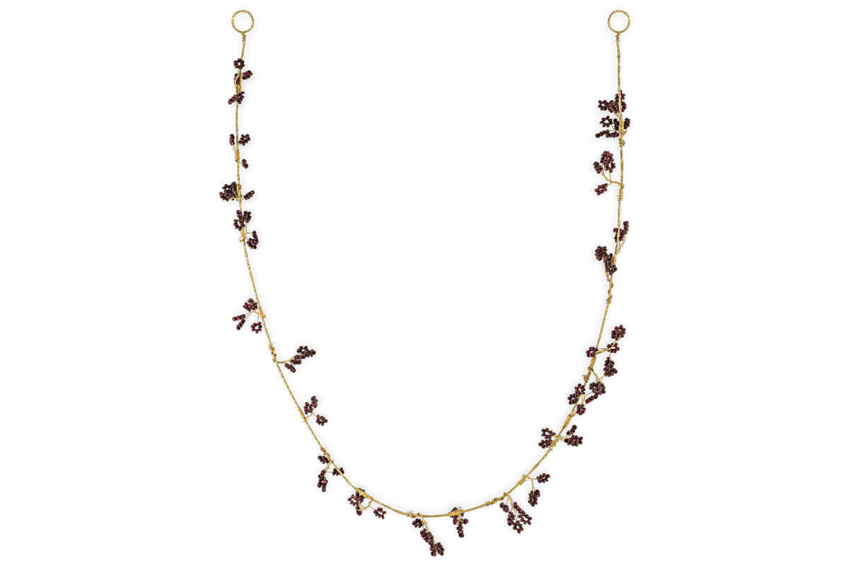 The nkuku Tanu Mango Wood Beaded Garland features brass and ruby beads, artfully clustered along the strand for a whimsical, foliage-inspired look. Displayed in a gentle U shape against a plain white background.