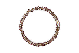 The Tanu Mango Wood Beaded Wreath by nkuku features brass and ruby beads arranged in a circular, organic pattern, creating a festive, textured look against a plain white background.