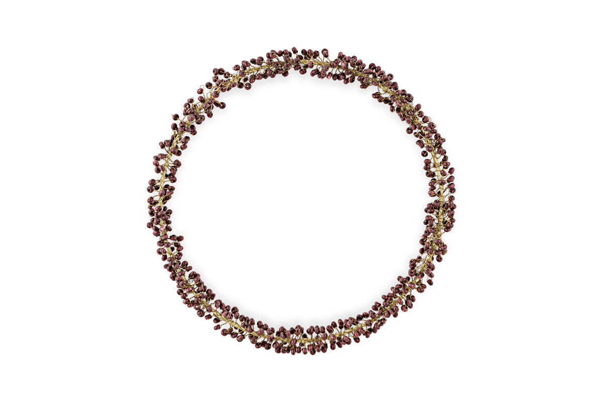The Tanu Mango Wood Beaded Wreath by nkuku features brass and ruby beads arranged in a circular, organic pattern, creating a festive, textured look against a plain white background.