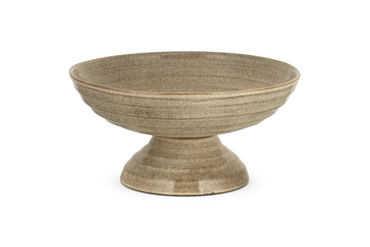 The Valinha Earthenware Footed Bowl by nkuku features a wide, shallow grey dish with a flared base and reactive glaze, ideal for enhancing rustic tablescapes. Displayed on a white background.