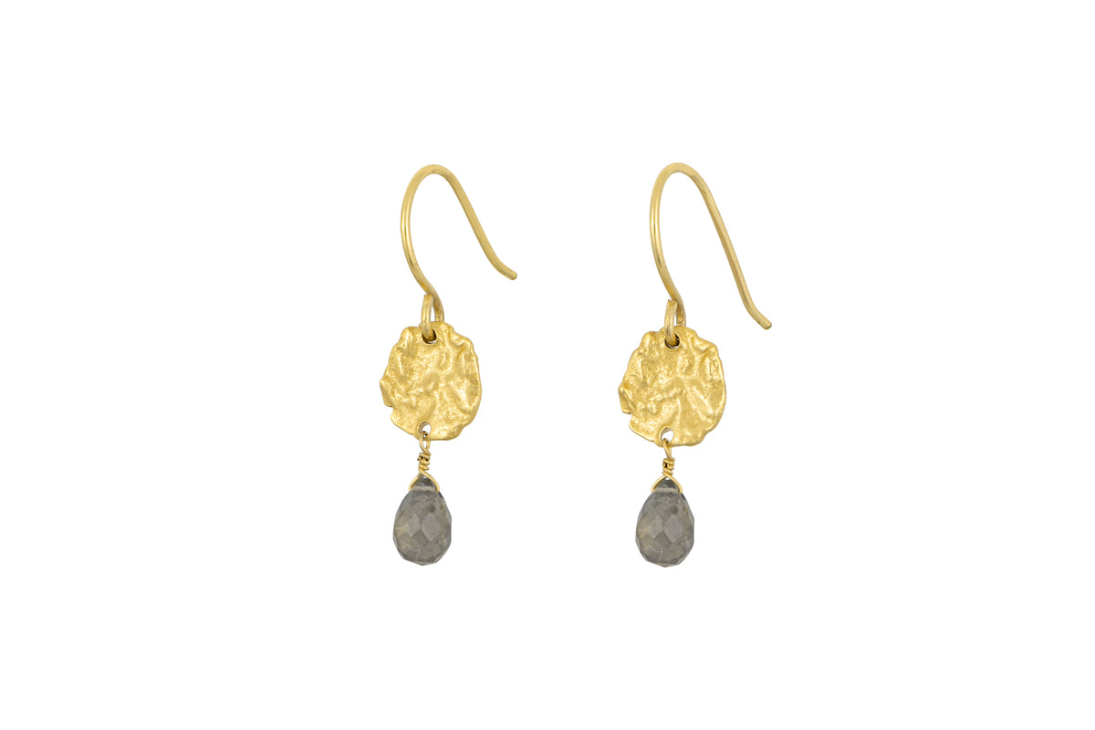 The Veera Labradorite Earrings - Gold by nkuku feature textured gold-toned discs with teardrop-shaped gray labradorite gemstones hanging below, set against a white background.