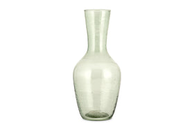 The Yala Hammered Jug - Sage Green by nkuku is a tall, clear glass jug with a narrow neck and wider base, crafted from subtly textured, slightly green-tinted recycled glassware.
