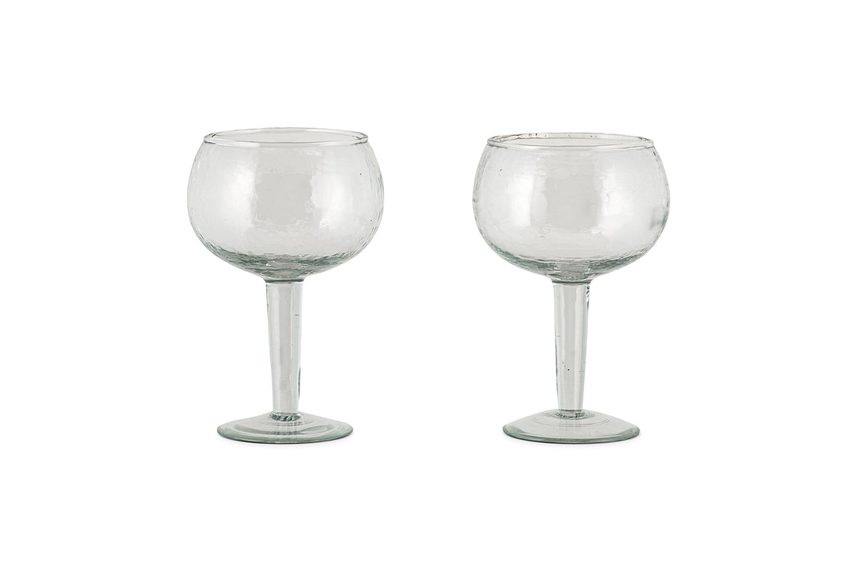 Two clear Yala Hammered Gin Glasses by nkuku, featuring round bowls and long stems, are displayed side by side on a white background. Set of 2.