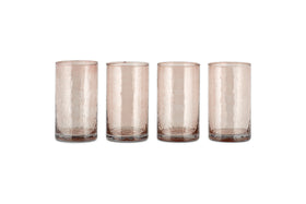 A set of four Yala Hammered Highball glasses by nkuku, made from recycled glass in a dusty terracotta hue, are arranged in a row on a white background.