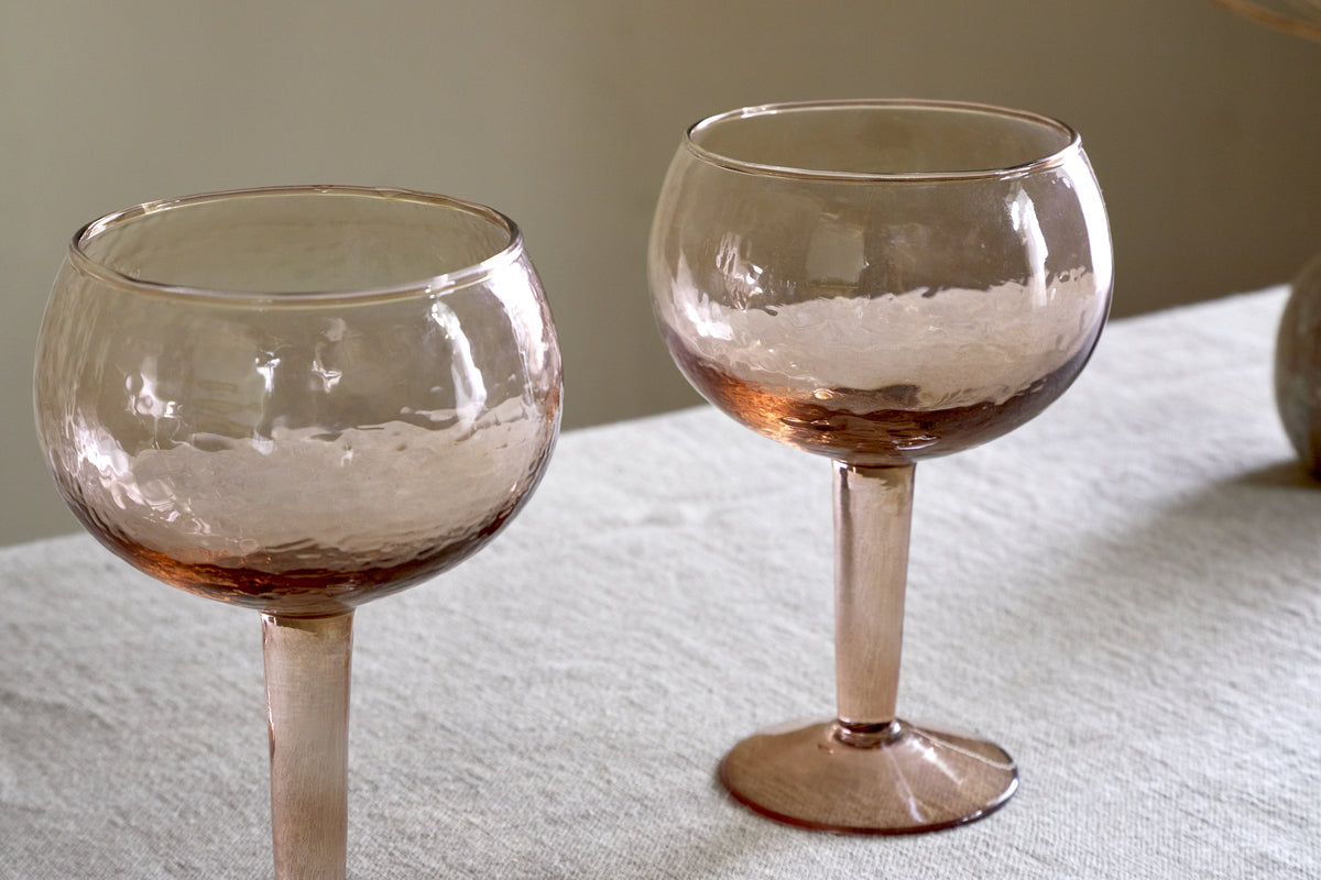 A set of two nkuku Yala Hammered Gin Glasses in Dusty Terracotta sits on a light tablecloth against a neutral background.