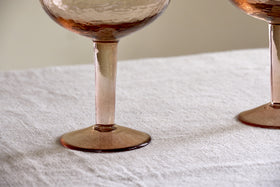 Two Yala Hammered Gin Glasses in Dusty Terracotta by nkuku sit on a light, textured fabric surface, showing only the hammered lower bowls.