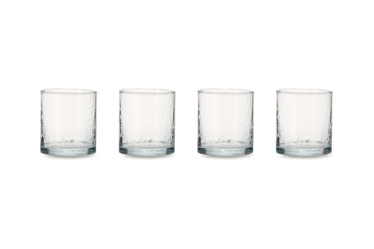 The nkuku Yala Hammered Tumbler set includes four clear, cylindrical glass tumblers with a dimpled, textured surface arranged in a row, highlighting their simple, modern design. Ideal for adding an organic touch to your tableware.