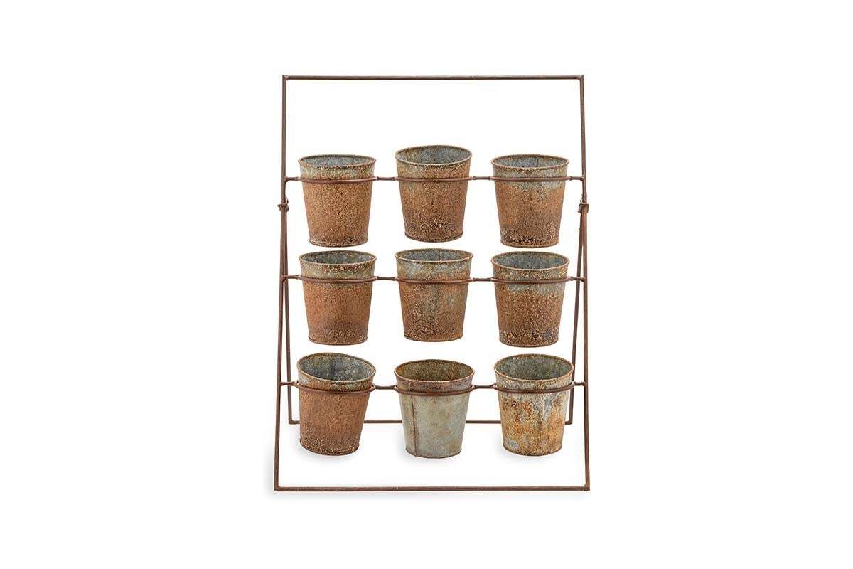 The Abari Planter Stand by nkuku holds nine rustic aged zinc pots in three rows. Angled backward for display, this minimalist metal rack showcases weathered pots—ideal as unique garden decor—against a plain white background.