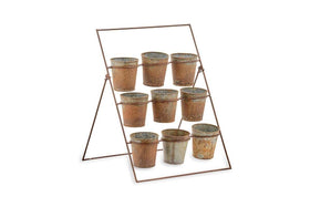 The nkuku Abari Planter Stand features three metal bars holding nine small, aged zinc pots with handles and unique patinas, arranged in a grid to create distinctive garden decor against a plain white background.