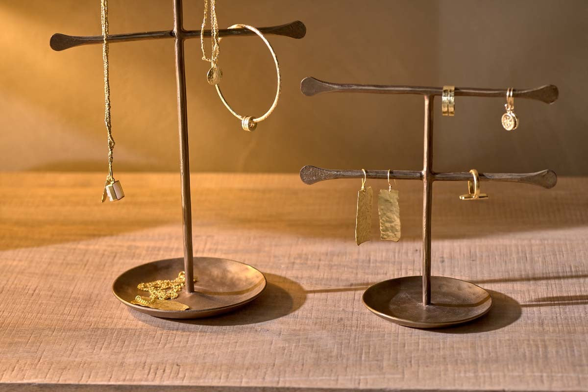 Two nkuku Liman Jewellery Stands display gold necklaces, bracelets, rings, and earrings on a wooden surface. Soft, warm lighting highlights the metallic textures and elegant details of each piece.
