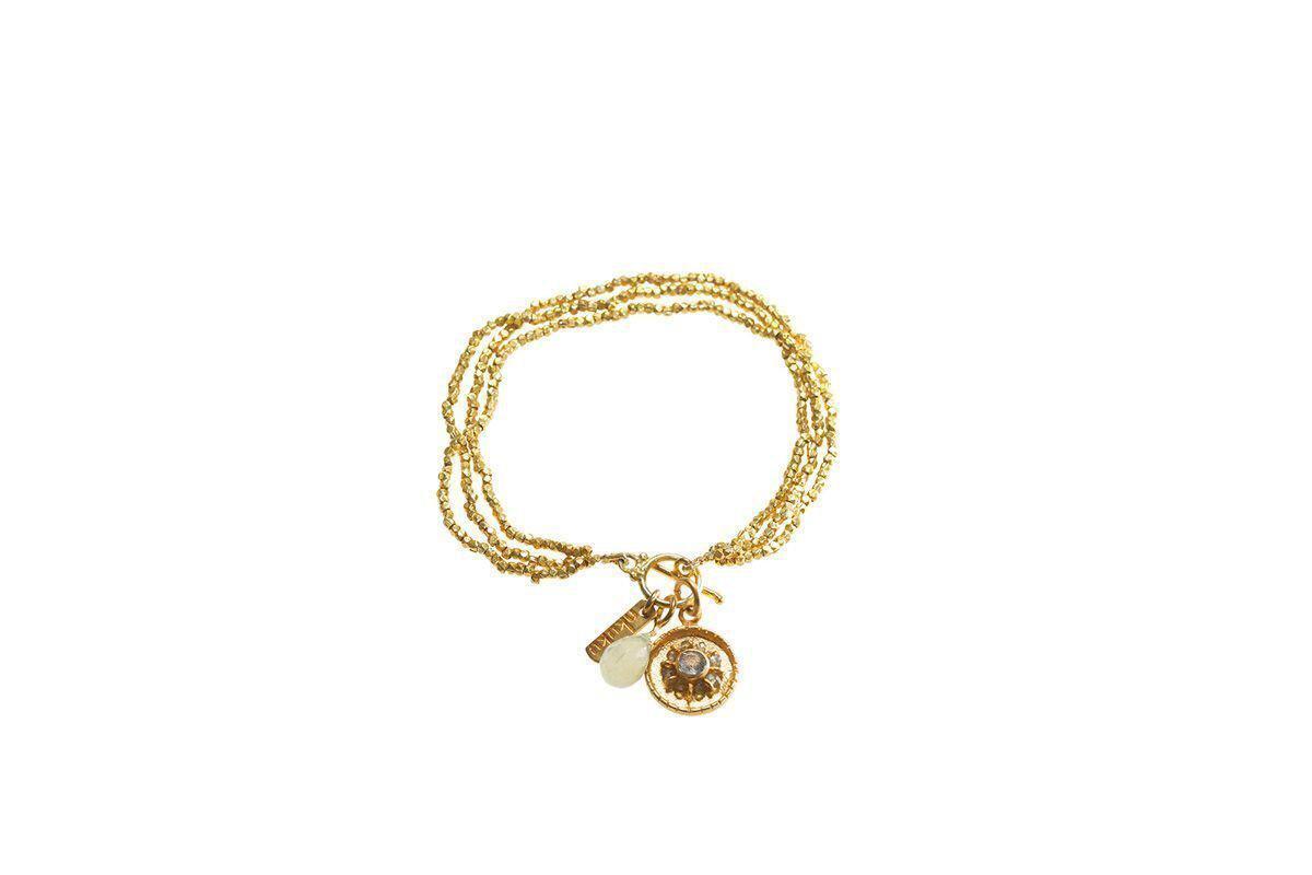 The Pandita Charm Bracelet by nkuku is a handmade gold-plated piece with three circular strands, adorned with a white stone, a small gold tag, and an intricate star medallion—an elegant addition to any jewelry collection.