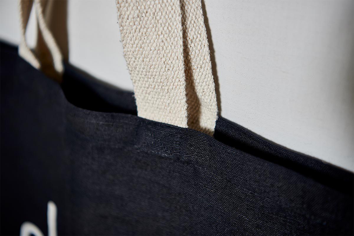 A close-up of nkuku's Jute & Cotton Tote Bag shows its black fabric and thick, textured beige handles stitched to the top edge—highlighting quality craftsmanship and a stylish choice for shopping.